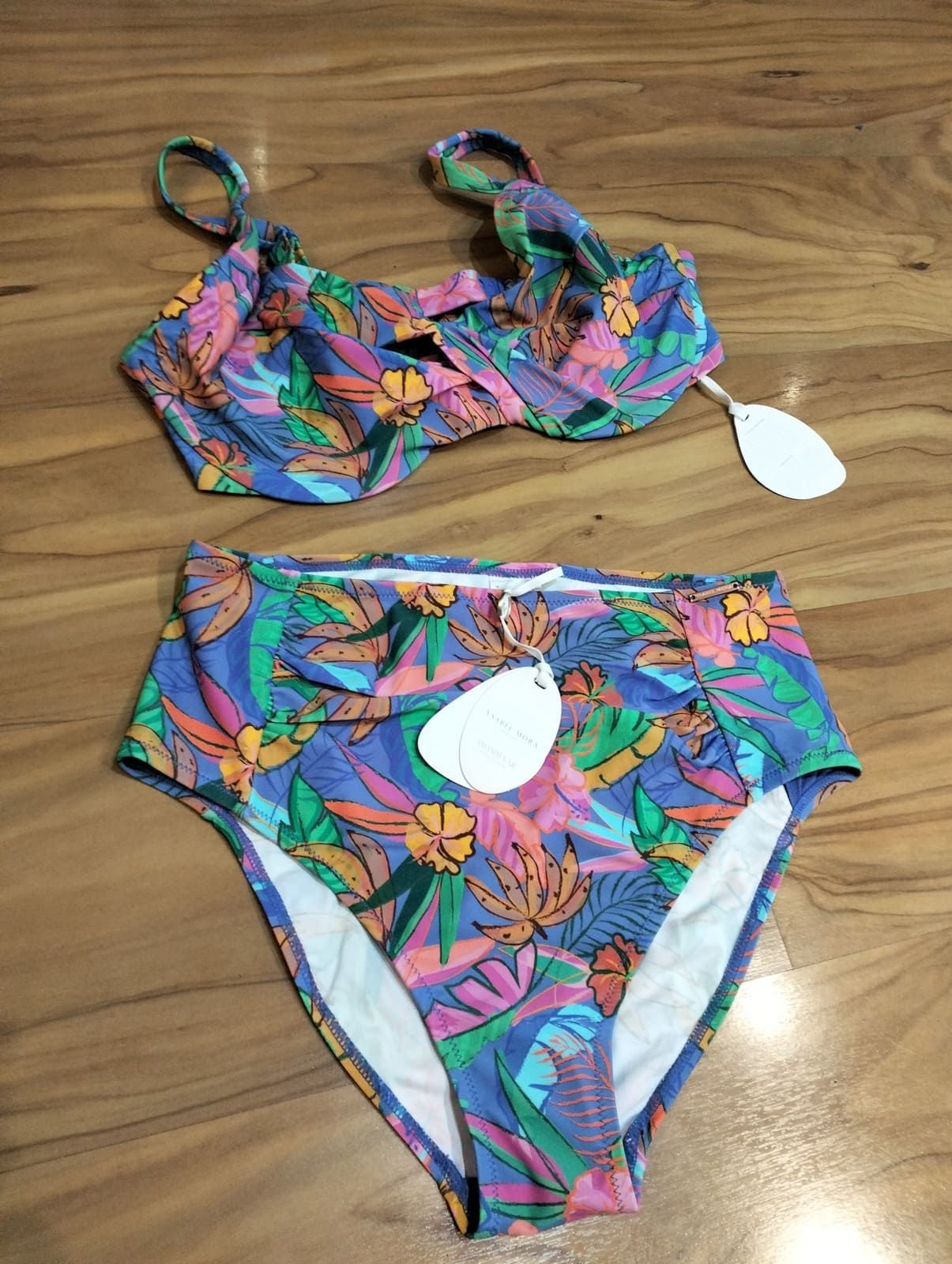 Un conjunto de bikini con estampado floral colorido, con braguita de talle alto y parte superior con aros, extendido sobre una superficie con textura de madera.