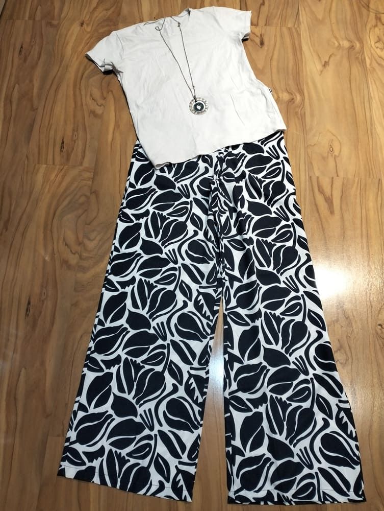 Un vestido de verano blanco, sin mangas, de largo midi, con ribete de encaje y detalles escalonados, extendido sobre un suelo de madera clara.
