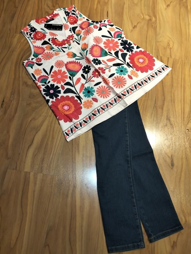 Un vestido de verano blanco, sin mangas, de largo midi, con ribete de encaje y detalles escalonados, extendido sobre un suelo de madera clara.