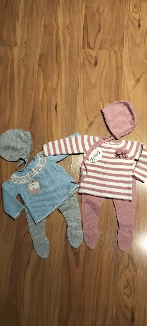 Dos muñecas bebé con ropa de punto tumbadas en un suelo de madera, cogidas de la mano