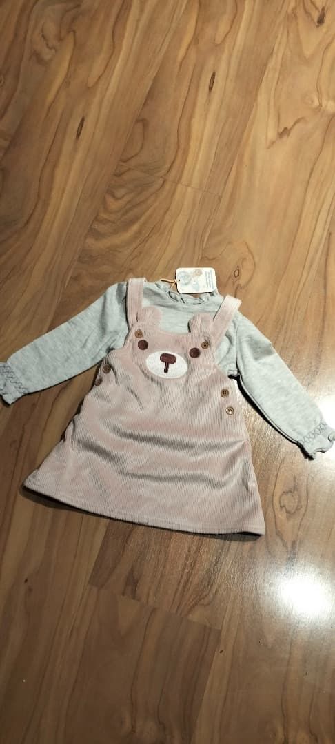 Vestido gris claro de bebé, de manga larga y con una carita de osito, sobre un suelo de madera