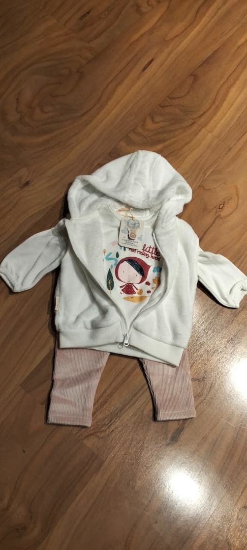 Sudadera blanca de bebé con capucha y pantalones de rayas extendidos sobre un suelo de madera.