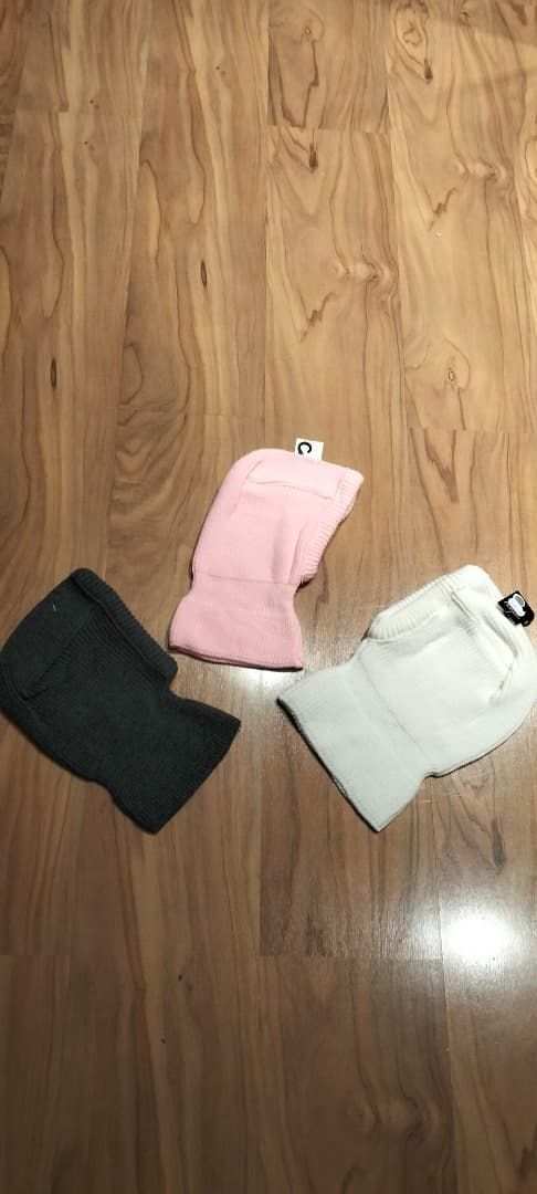 Tres camisas dobladas en un suelo de madera: negra, rosa y blanca.
