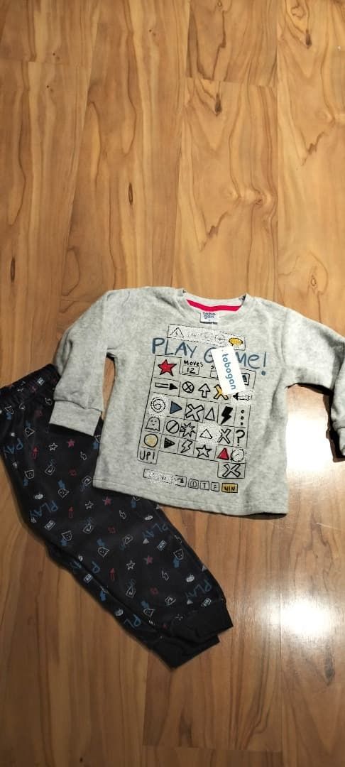 Conjunto de dos piezas sobre suelo de madera: camiseta gris de manga larga con estampado y pantalones oscuros estampados