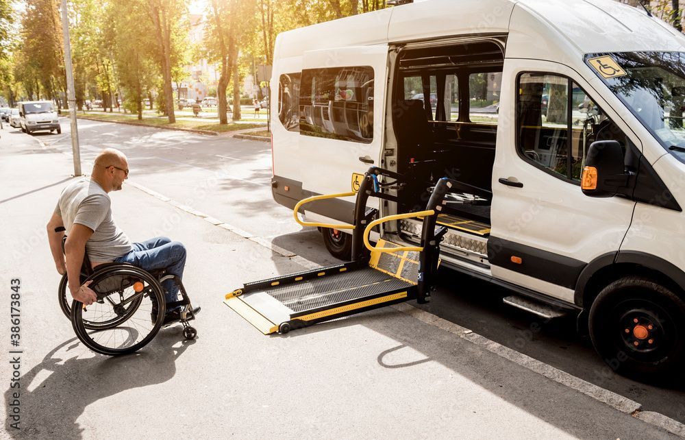 Eine Person im Rollstuhl nähert sich auf einer sonnigen Strasse einem Lieferwagen mit offener Rampe.