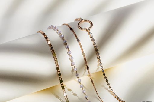 Mehrere filigrane Armbänder aus Gold und Silber liegen dekorativ auf einer hellen Oberfläche mit weichen Schatten. Mehrere filigrane Armbänder aus Gold und Silber liegen dekorativ auf einer hellen Oberfläche mit weichen Schatten.