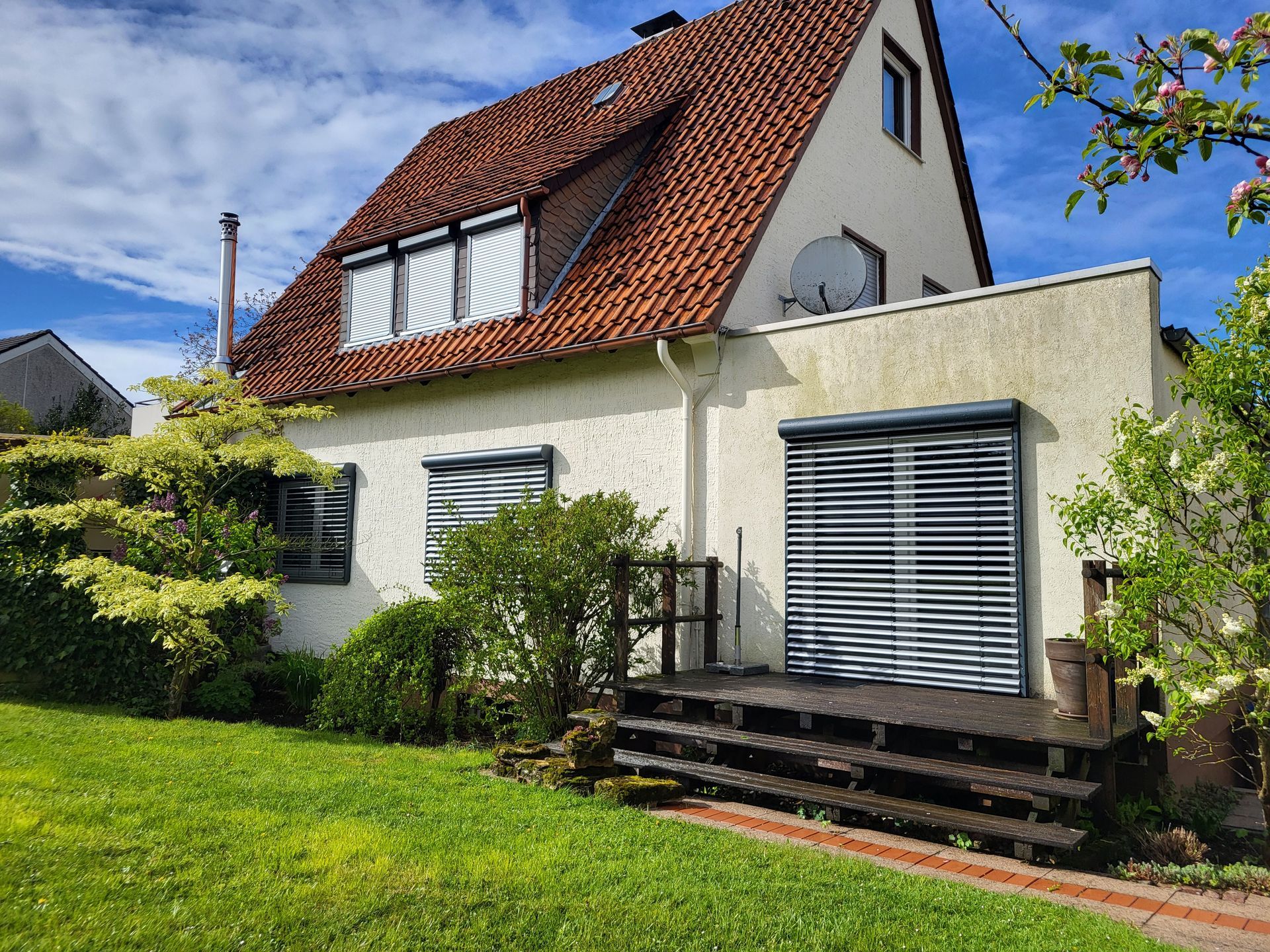 Zweistöckiges Haus mit rotem Ziegeldach, weißen Wänden und einem grünen Rasen vor den Fensterläden.