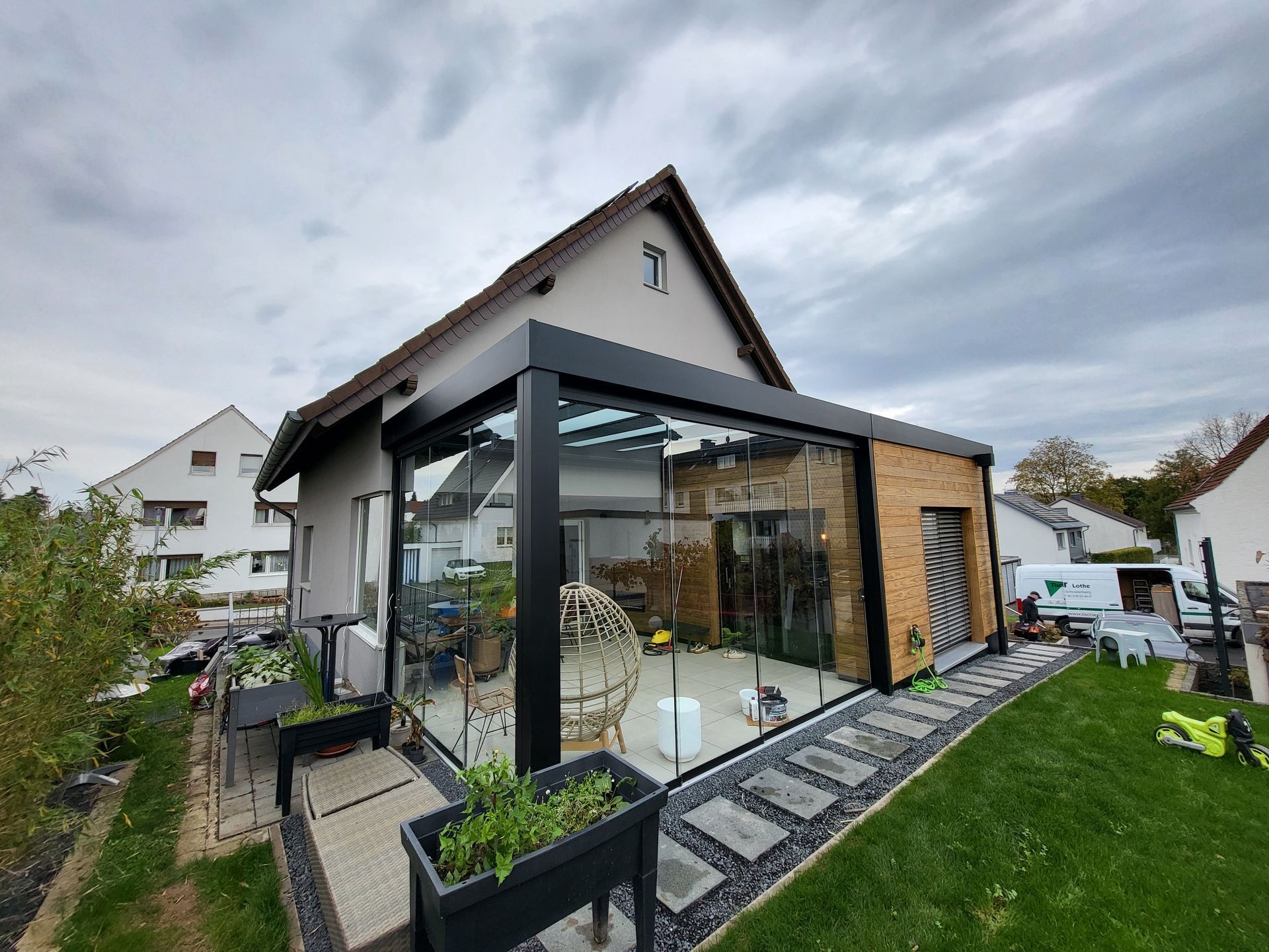 Modernes Haus mit gläsernem Wintergarten und angelegtem Garten unter bewölktem Himmel