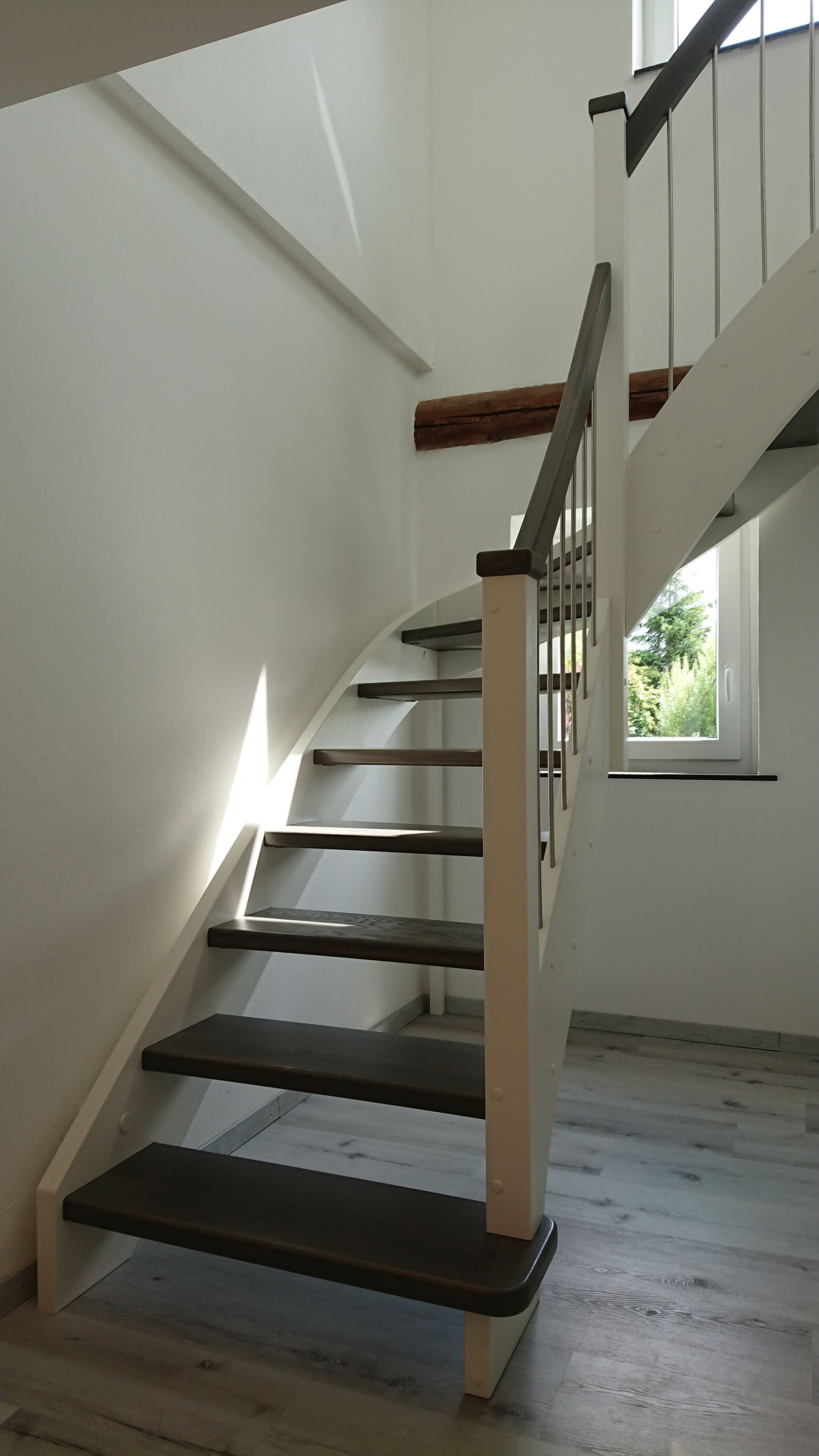 Moderne Innentreppe mit Holzstufen, dunklen Trittstufen und weißen Wänden an einem Fenster.