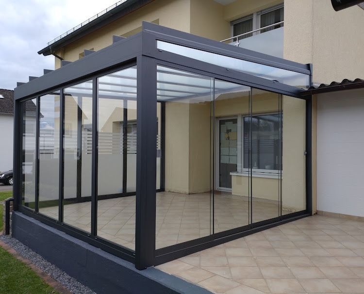 Verglaster Terrassenwintergarten, an ein Haus angebaut, mit dunklem Metallrahmen und Fliesenboden
