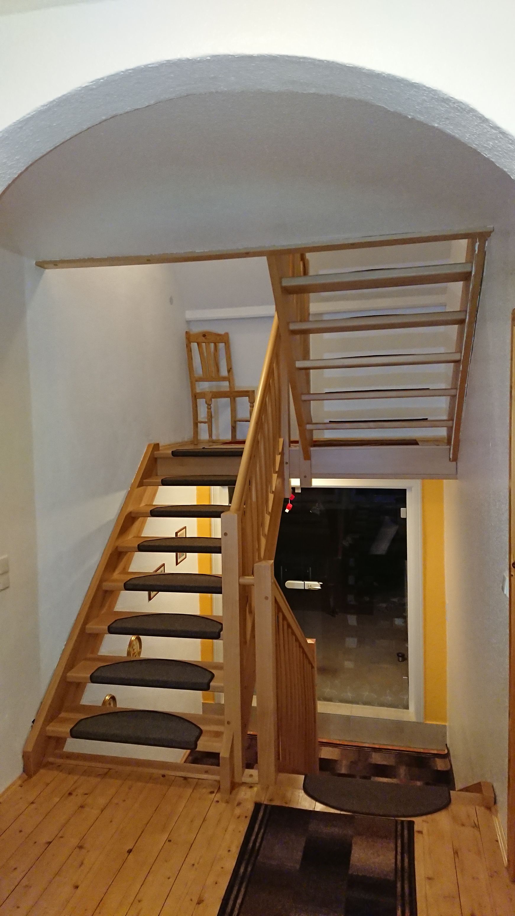 Holztreppe mit weißen Wänden und einem Geländer zum Dachboden in einem kleinen Eingangsbereich.
