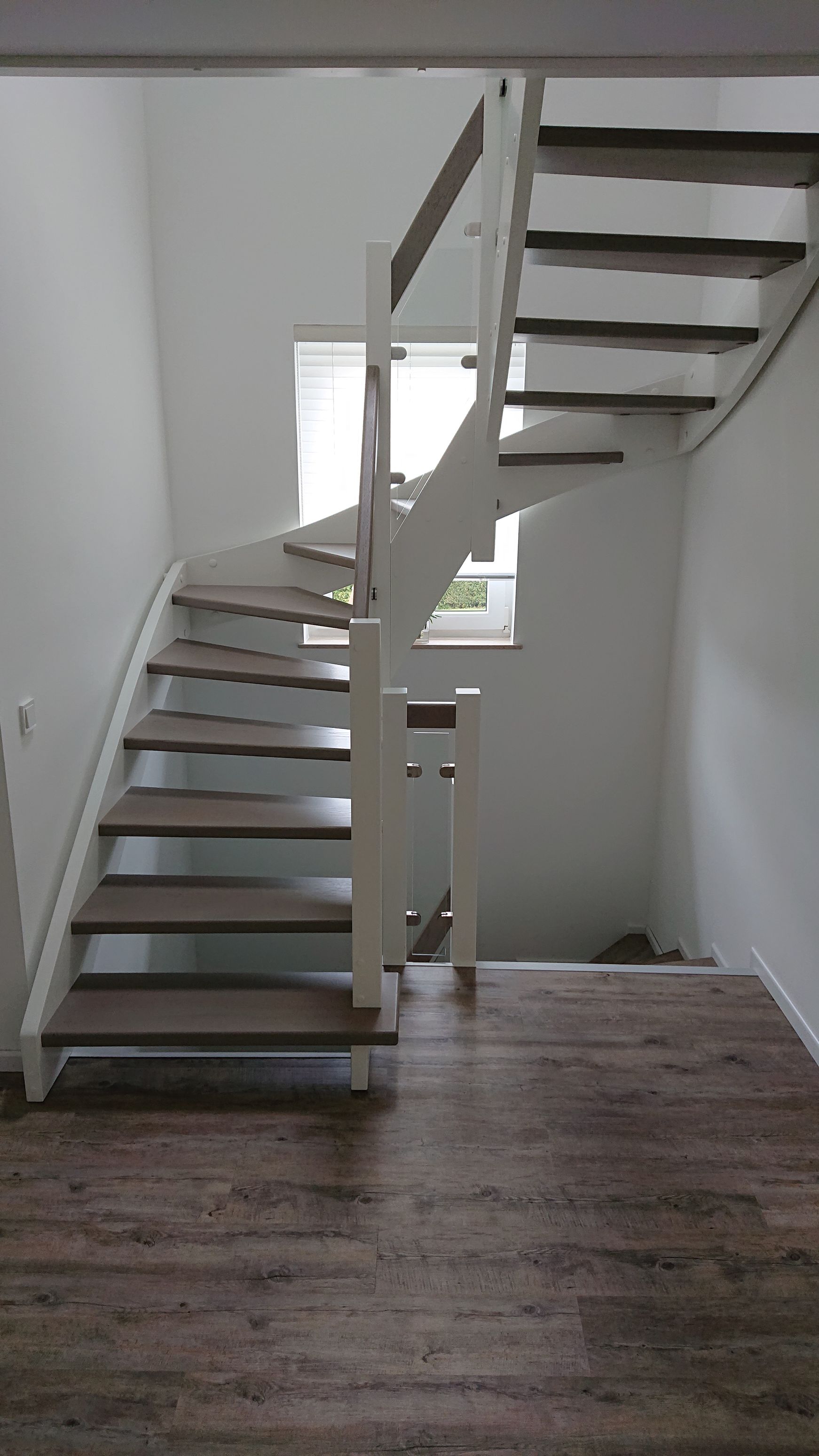 Geschwungene Innentreppe mit weißem Geländer und dunklen Holzstufen in einem minimalistischen Raum