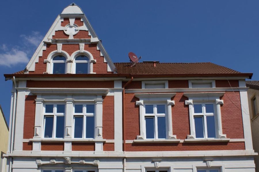 Historisches Backsteingebäude mit weißen Verzierungen und steilem Giebeldach vor blauem Himmel