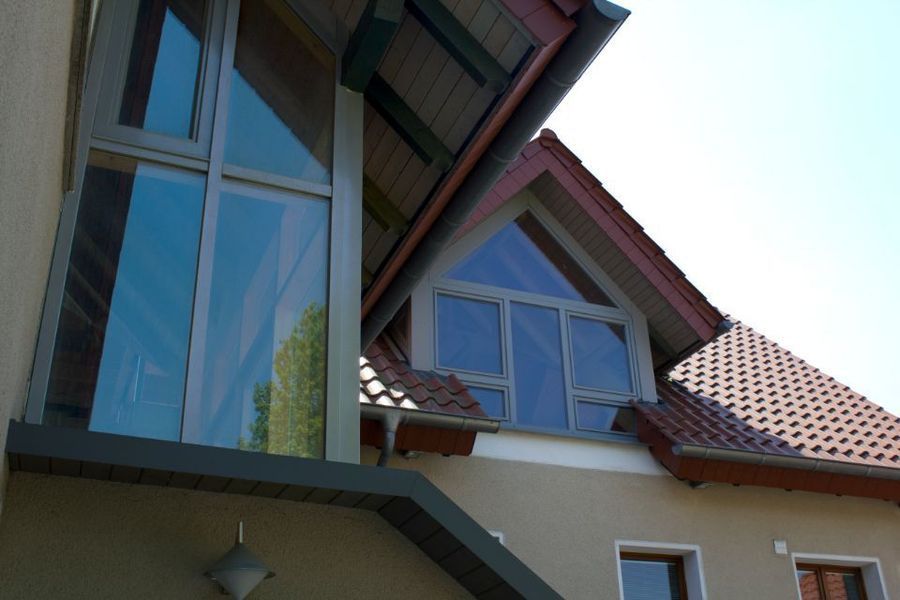 Außenansicht eines Hauses mit hohen blauen Fenstern und einem roten Ziegeldach unter klarem Himmel