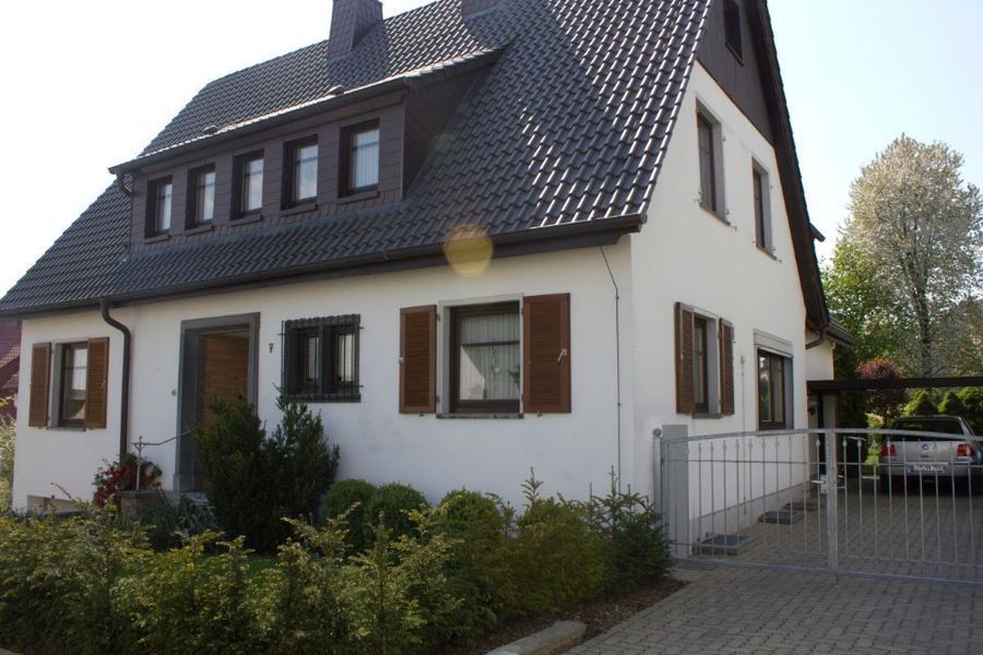 Weißes Haus mit dunklem Dach, braunen Fensterläden und einem Einfahrtstor in ruhiger Wohnlage