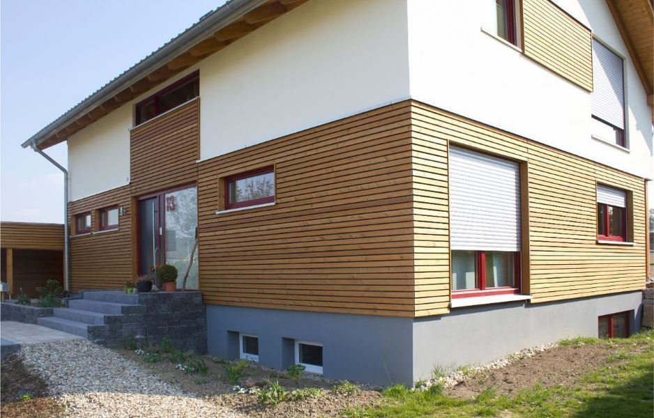Modernes Haus mit Holzverkleidung, weißen Wänden und kleinen Kellerfenstern entlang eines Kieswegs