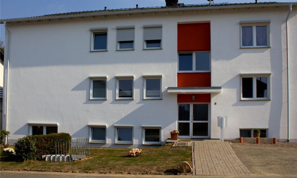 Modernes weißes Mehrfamilienhaus mit roten Akzenten und einem kleinen Vorgarten