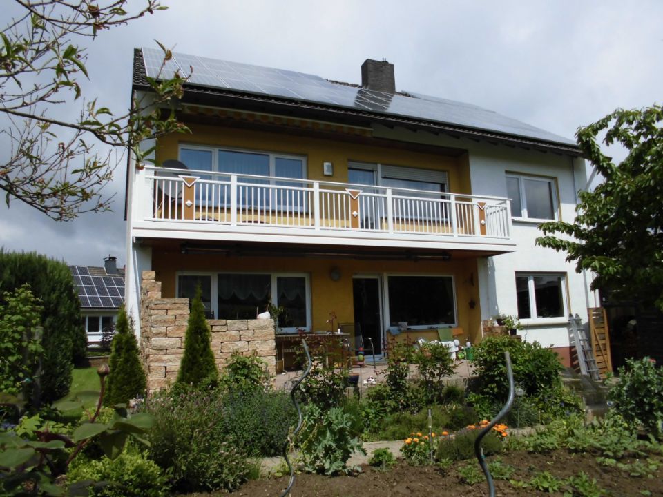 Zweistöckiges Haus mit weißem Balkon und üppigem Garten davor