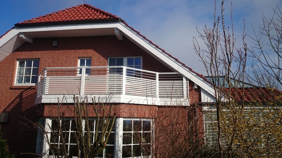Backsteinhaus mit rotem Dach und weißem Balkongeländer unter klarem, blauem Himmel
