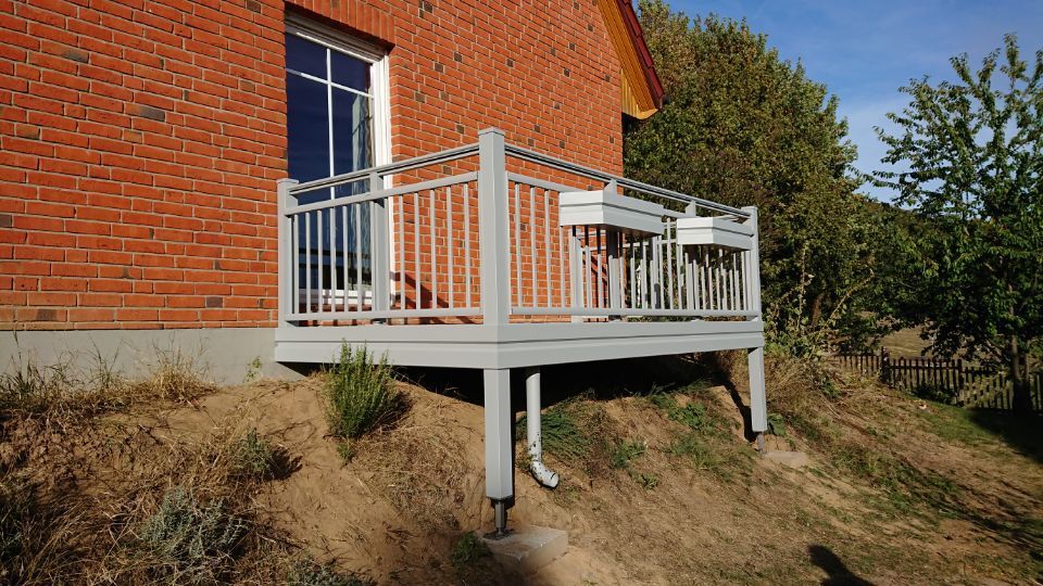 Veranda mit weißem Geländer, die an ein rotes Backsteinhaus an einem grasbewachsenen Hang angrenzt