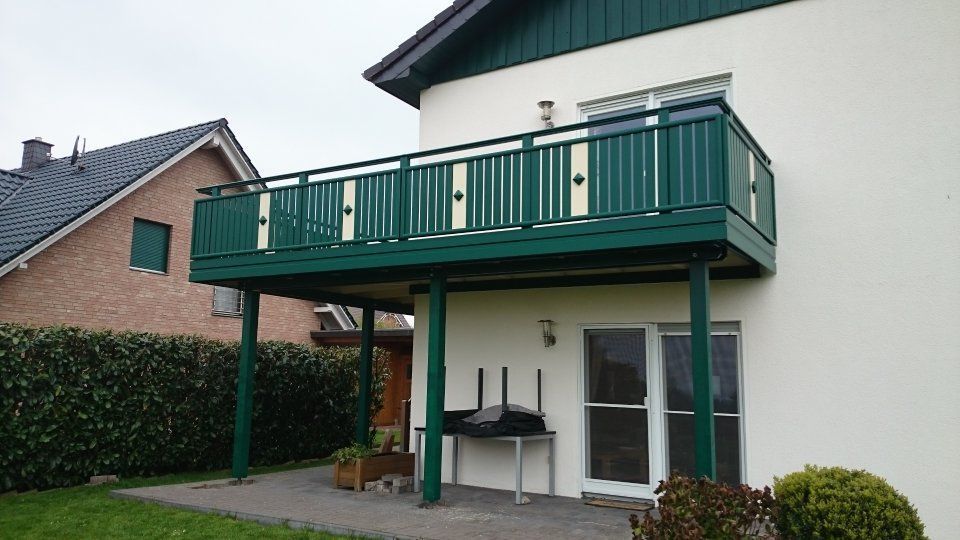 Hausfassade mit grünem Balkon, weißem Untergeschoss und Terrassenbereich unter dem Balkon