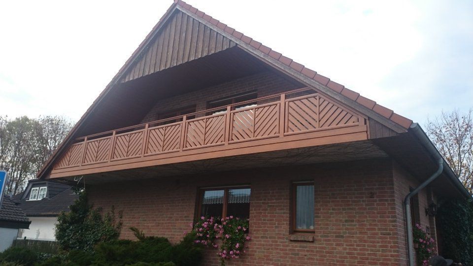 Backsteinhaus mit Holzbalkon und steilem Dach, von unten betrachtet.