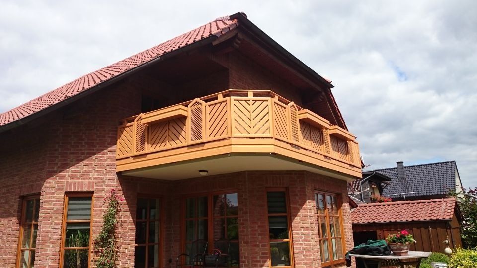 Zweistöckiges rotes Backsteinhaus mit orangefarbenem Balkon und Dach unter einem bewölkten Himmel