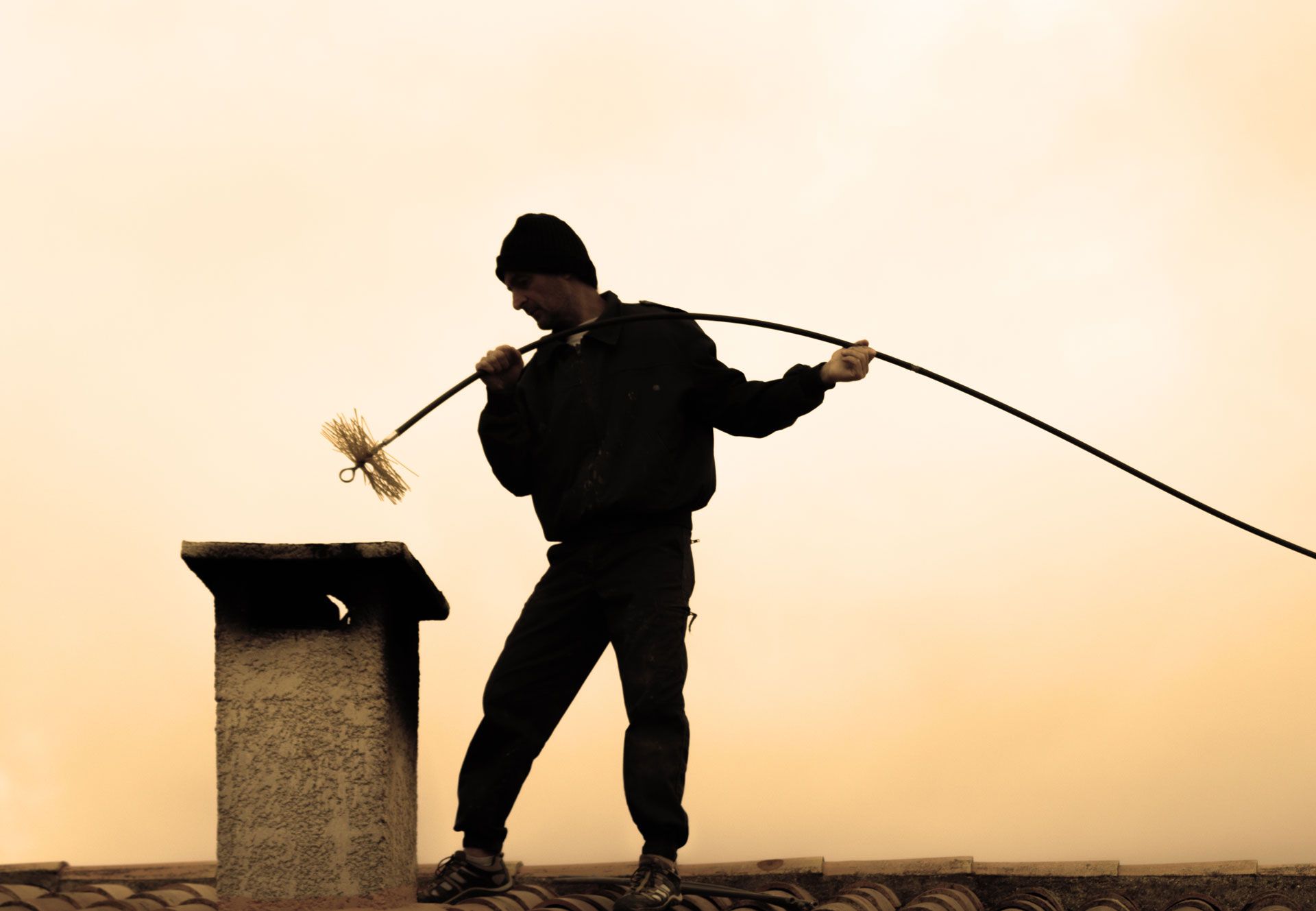 Un professionnel du ramonage sur un toit devant une cheminée