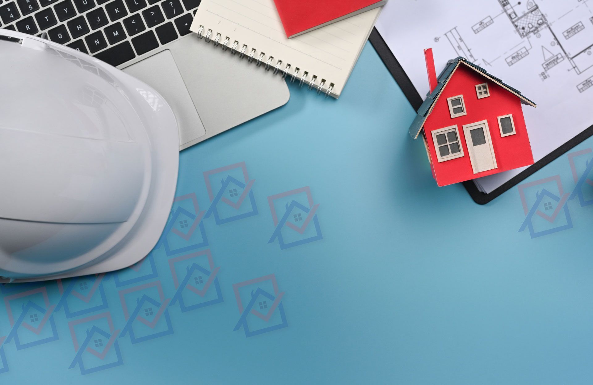 Un casque de chantier avec un clavier d'ordinateur et des plans d'architecte derrière une maquette de maison