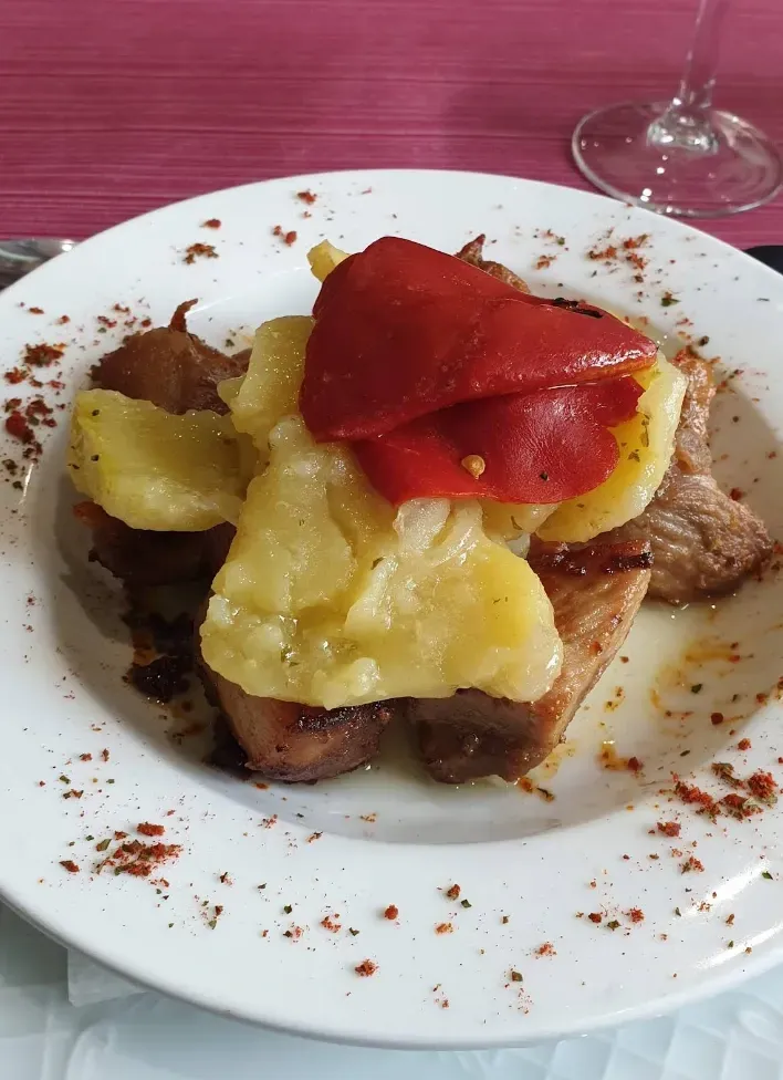 Plato con carne asada, patatas y pimientos rojos, espolvoreados con pimentón.