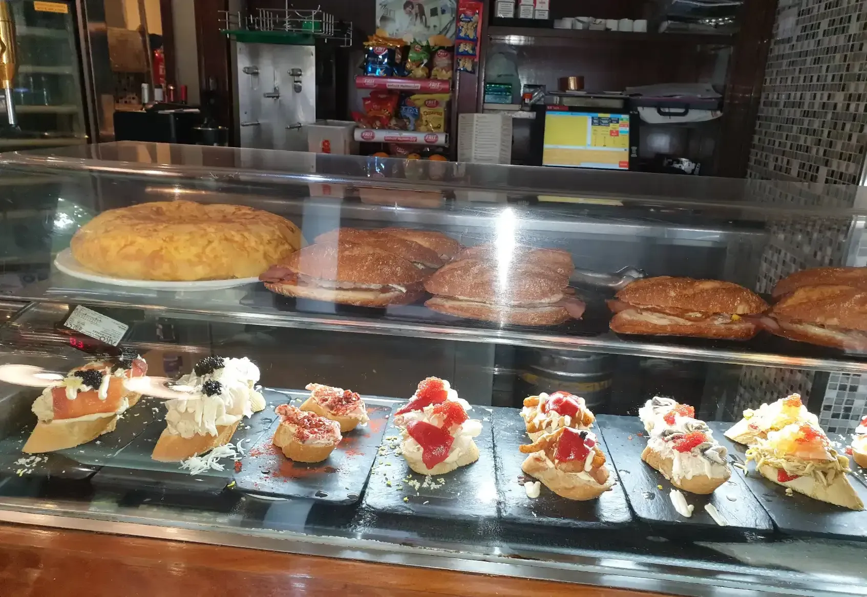 Vitrina con diversos bocadillos y tapas en una cafetería.