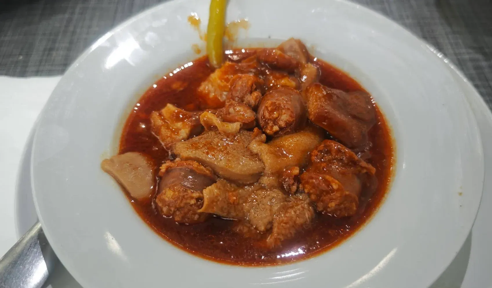 Callos y chorizo guisados en salsa roja, servidos en plato blanco.