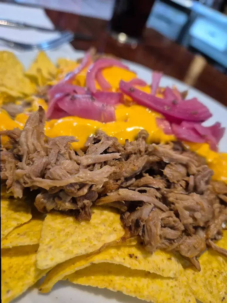 Nachos: chips de tortilla cubiertos con carne desmenuzada, salsa de queso y cebollas rojas encurtidas.