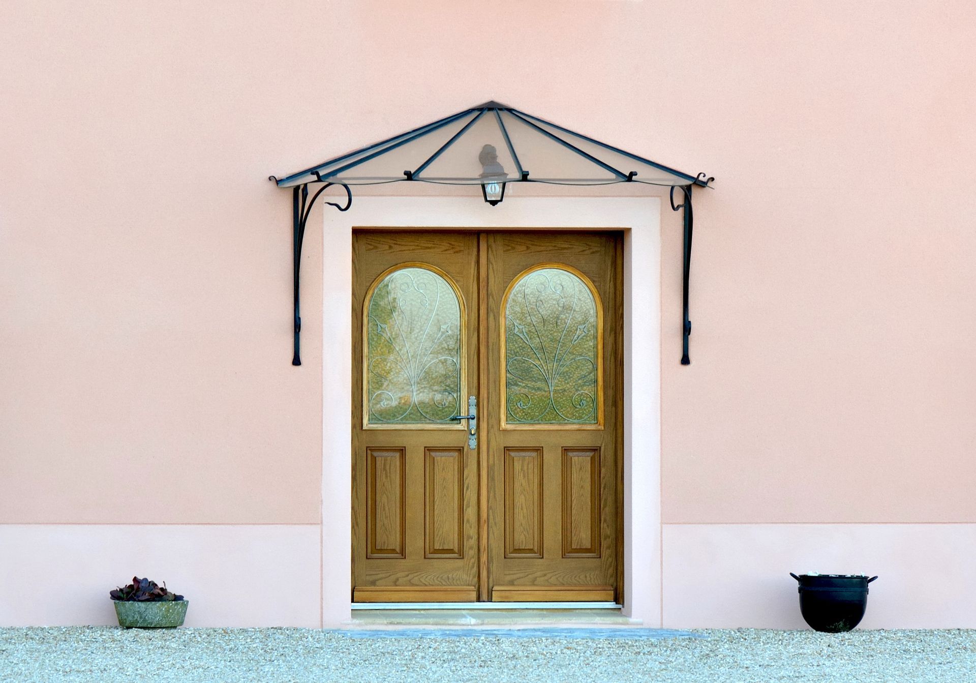 Porte d’entrée avec deux portes en bois, un petit auvent et deux jardinières contre un mur rose pâle