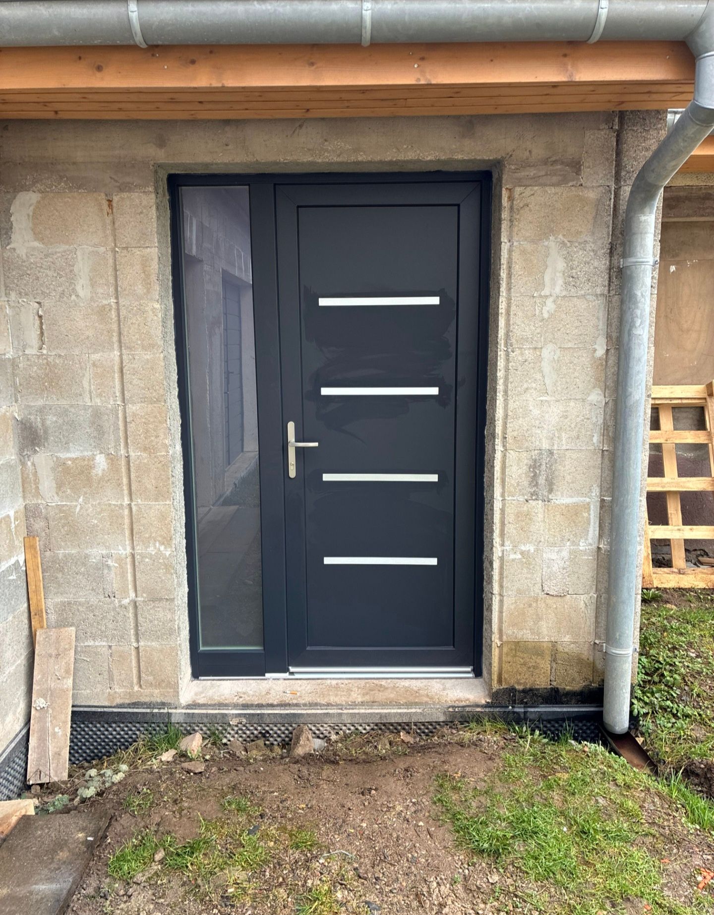 Porte d’entrée noire moderne avec des accents horizontaux blancs, intégrée dans un mur extérieur en pierre.