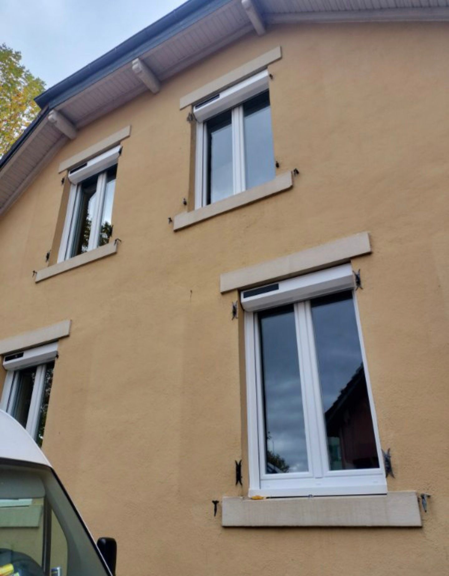 Façade d’une maison en stuc jaune avec plusieurs fenêtres à encadrement blanc et un toit en pente