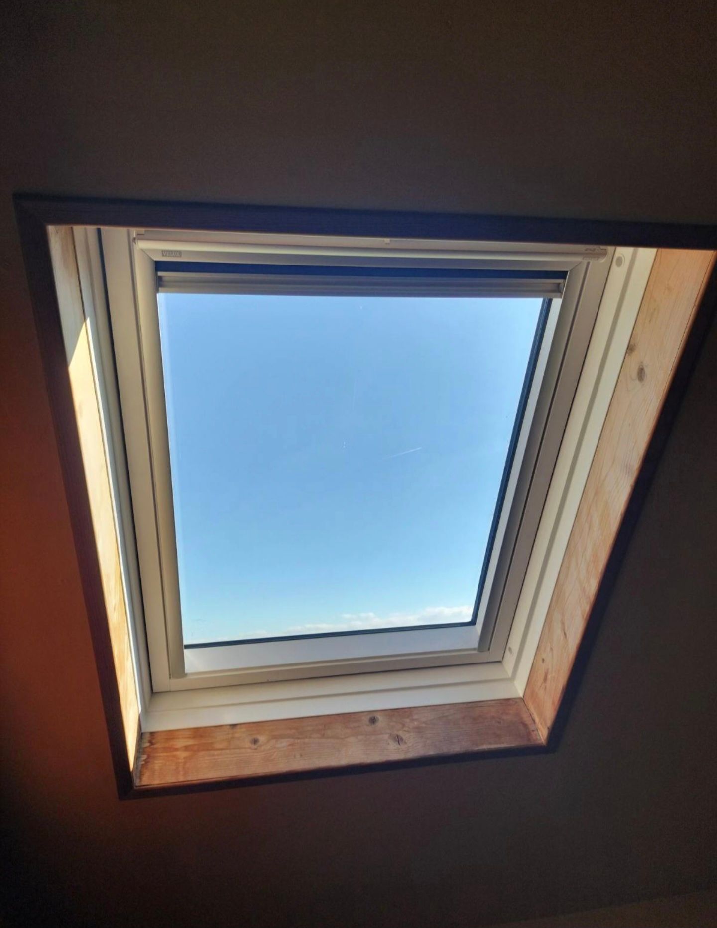 Fenêtre de toit intégrée dans un plafond incliné, laissant apparaître le ciel bleu et une bordure en bois.