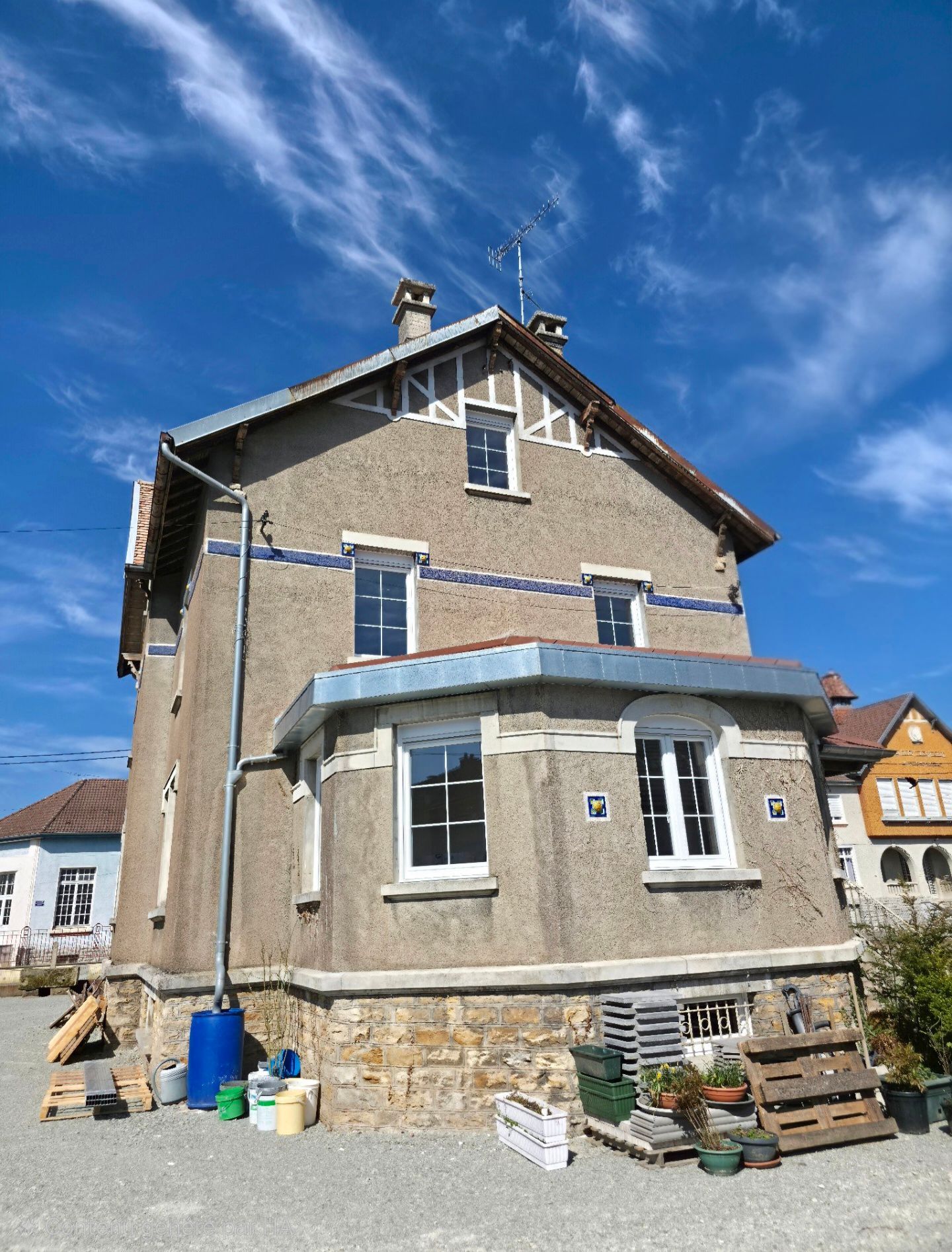 Maison en pierre à deux étages avec un petit porche et un auvent bleu sous un ciel d’un bleu éclatant