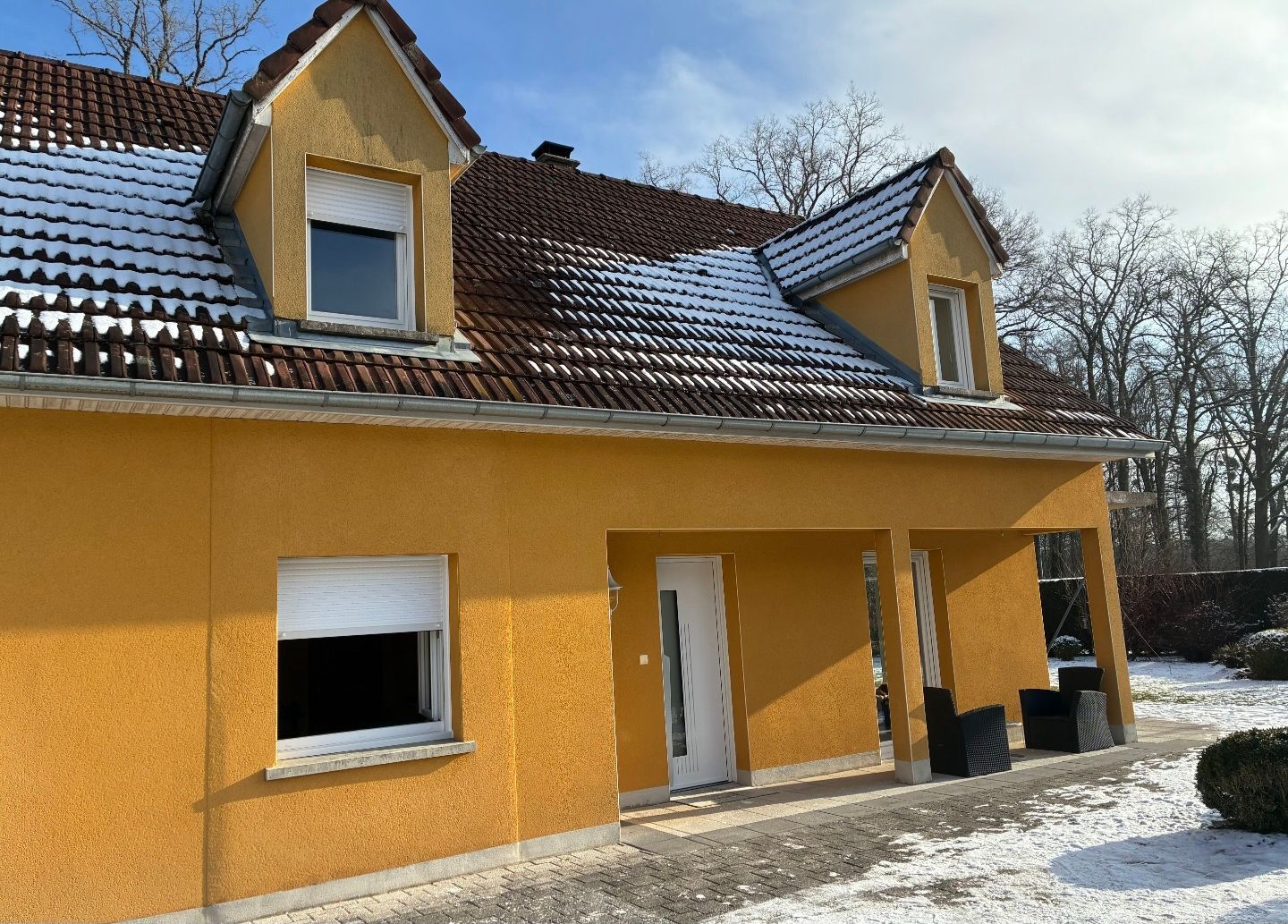 Maison jaune avec de la neige sur le toit et au sol, vue de l’extérieur par une journée d’hiver