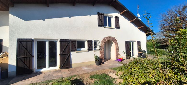 Maison blanche en stuc aux volets noirs, avec une porte d’entrée rose cintrée et un jardin devant