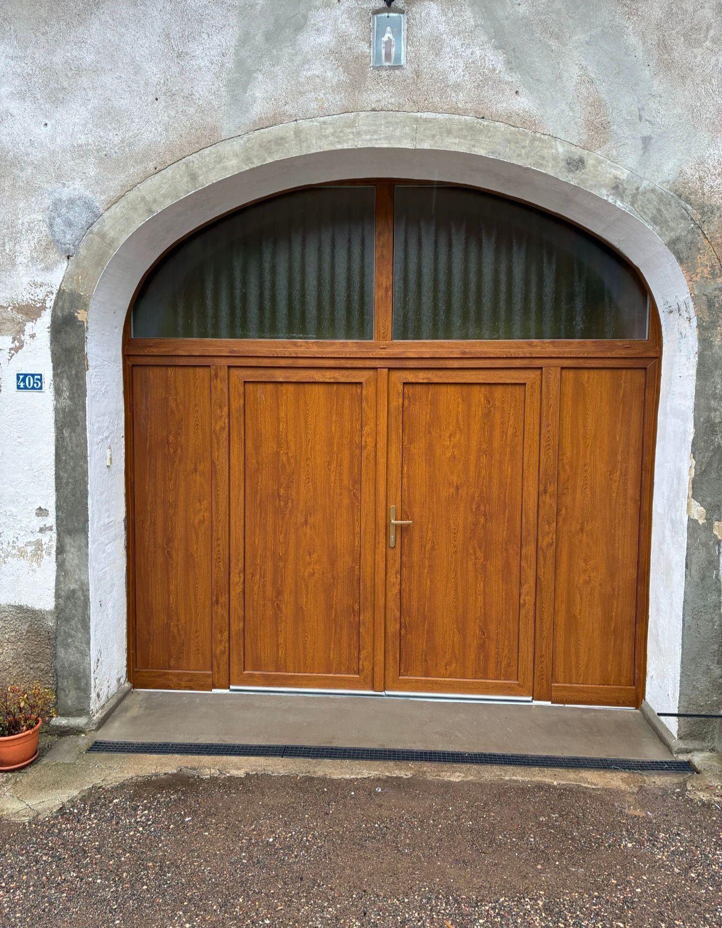 Porte de garage double en bois sous une arche en pierre, avec une petite fenêtre au-dessus