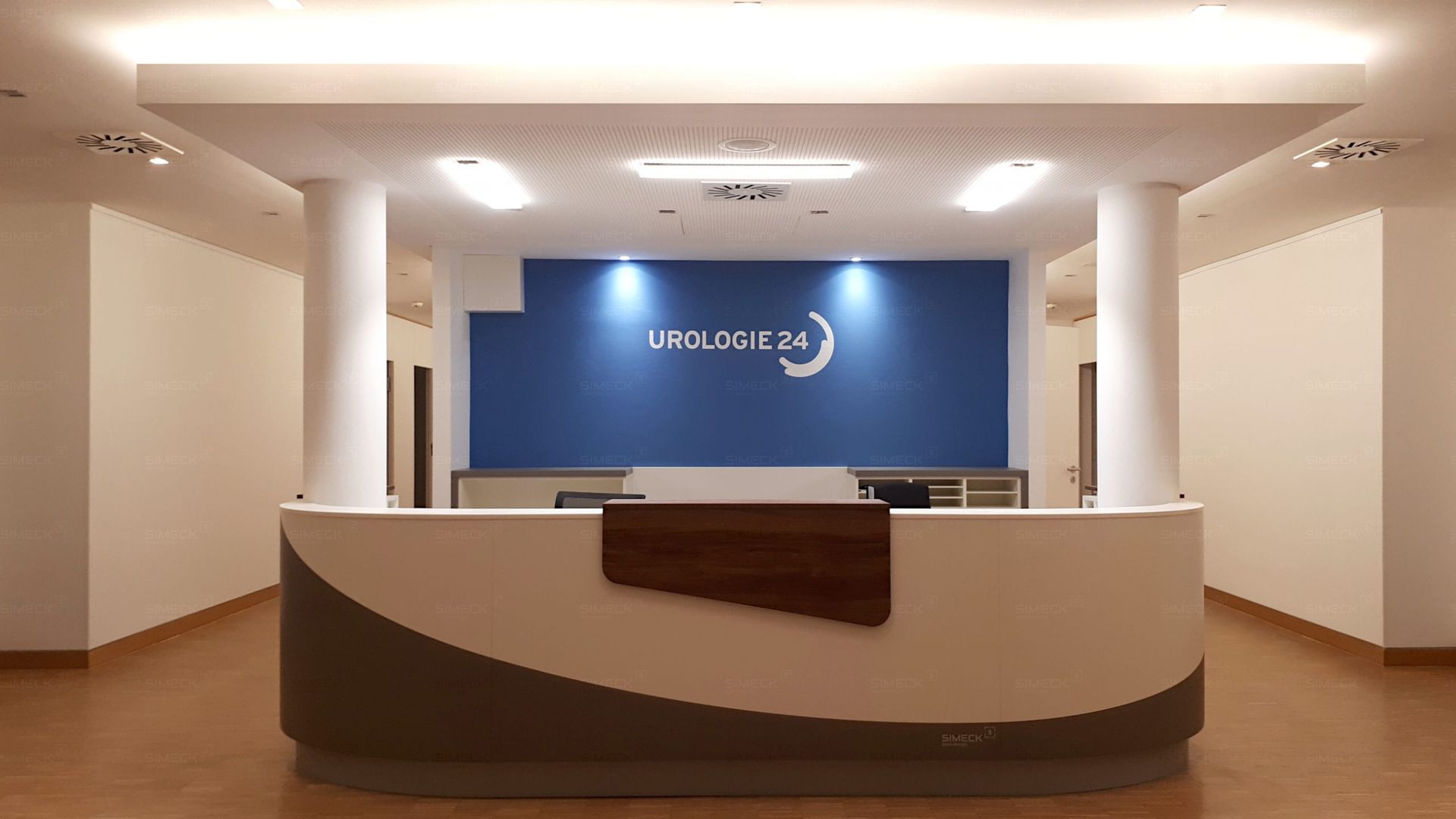 Ein Empfangsbereich mit einer blauen Wand und einem Schild mit der Aufschrift „Bitte warten“