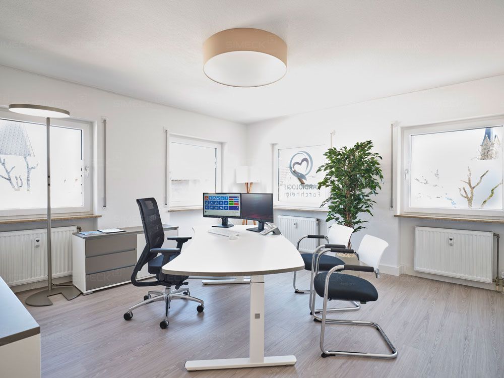 Ein Zimmer mit einem Schreibtisch, Stühlen und einem Computer darauf.