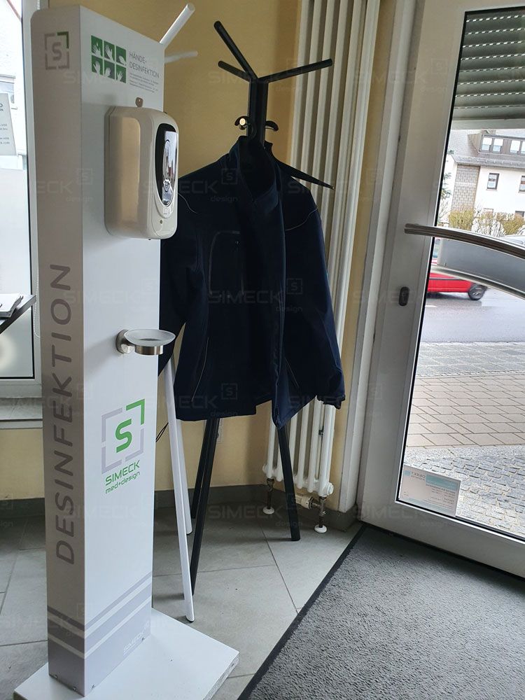 Ein Mantel, der auf einem Ständer neben einem Spender für Händedesinfektionsmittel hängt