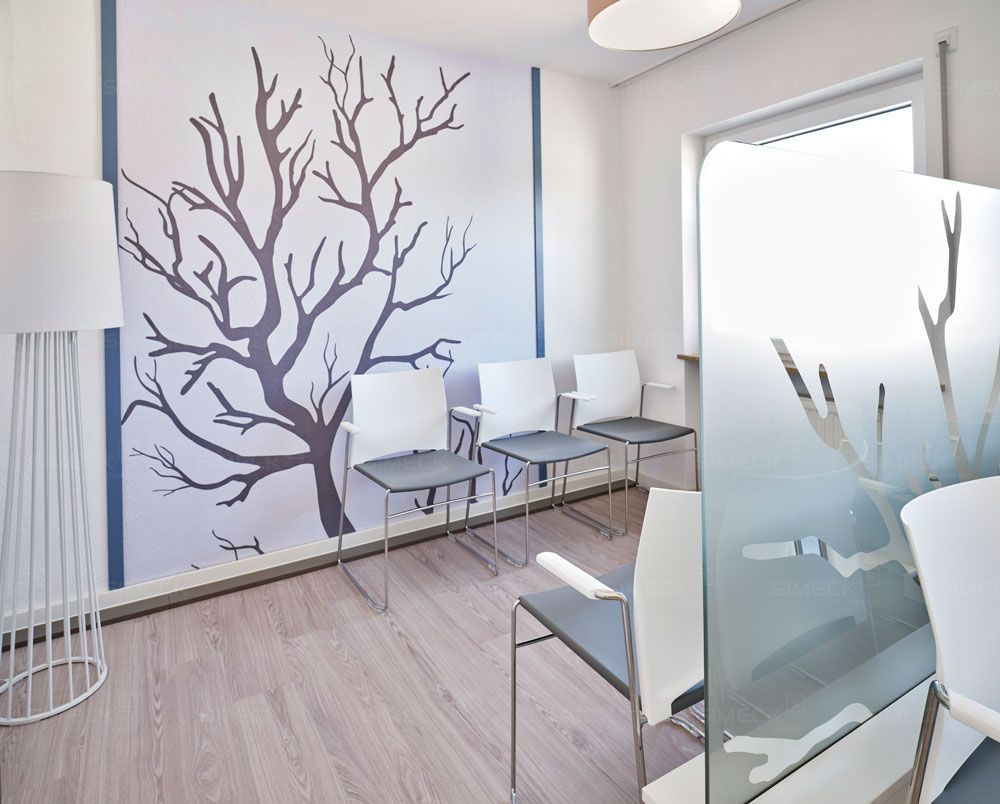 Ein Wartezimmer mit Stühlen und einem Baum an der Wand.