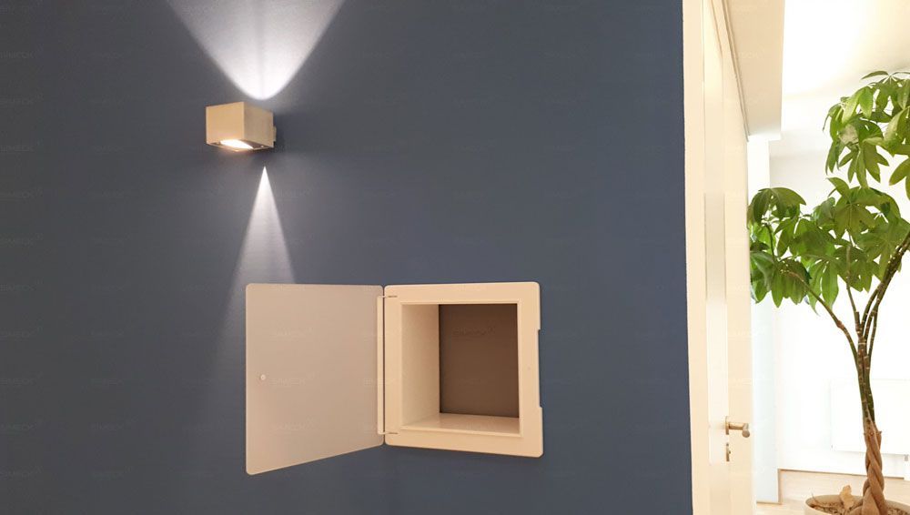 An einer blauen Wand steht neben einer Pflanze ein weißer Kasten.