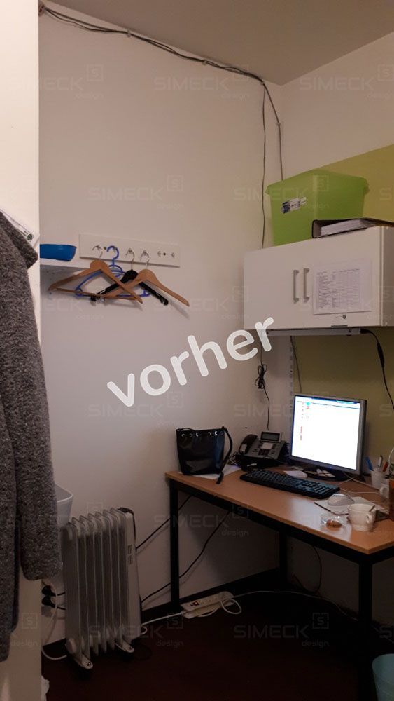 Ein Zimmer mit Schreibtisch, Computer, Telefon und Heizung.