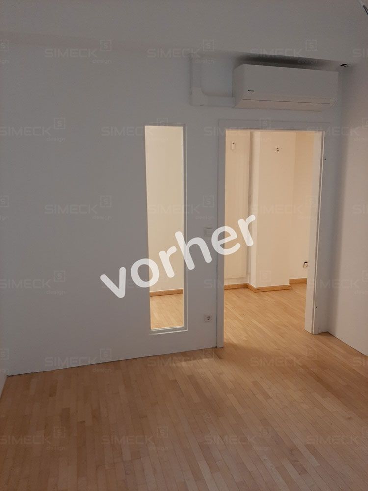 Ein Raum mit Holzboden und einer weißen Wand, auf der das Wort „Vorher“ steht.