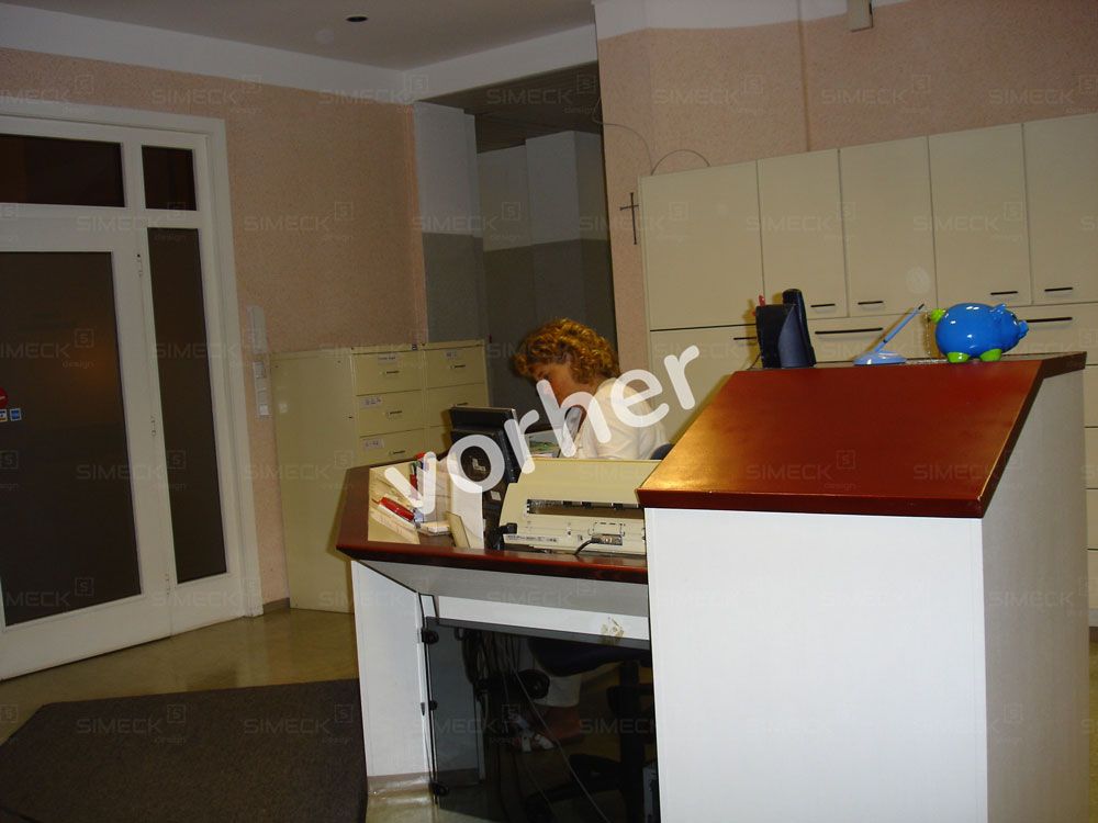 Eine Frau sitzt an einem Schreibtisch vor einem Schild mit der Aufschrift „vorher