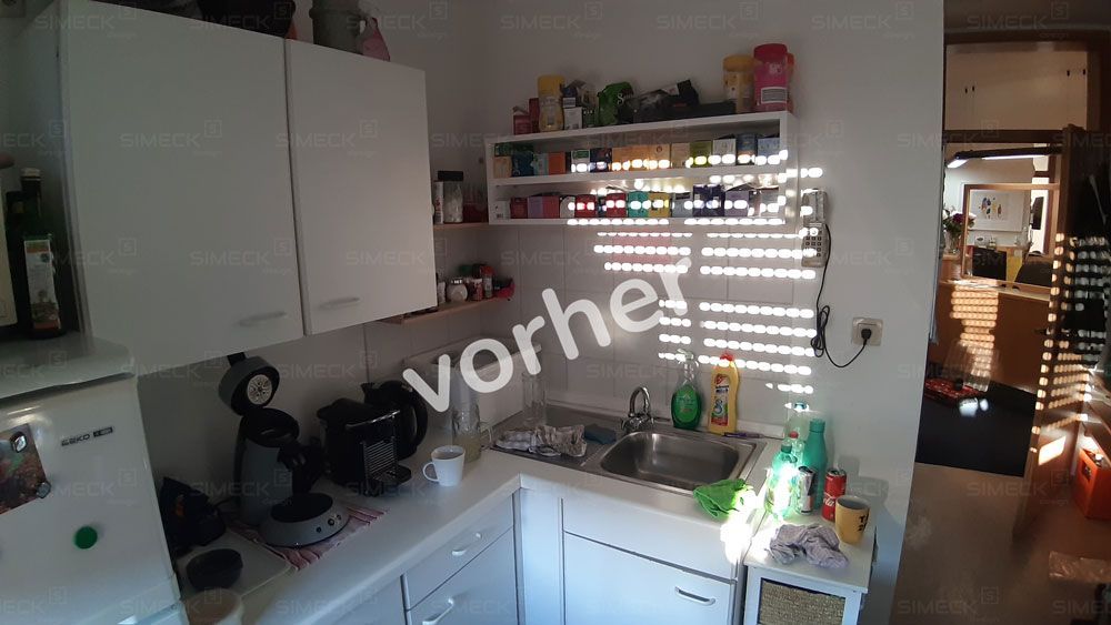 Eine Küche mit weißen Schränken, einer Spüle, einem Kühlschrank und einem Fenster.